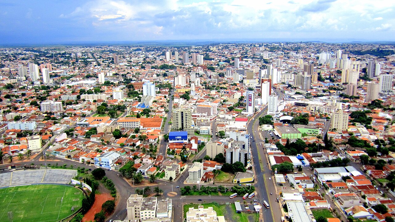 Vista aérea de Uberaba, Minas Gerais, com prédios do centro, casas de telhado cerâmico, avenidas e um estádio de futebol no canto inferior esquerdo